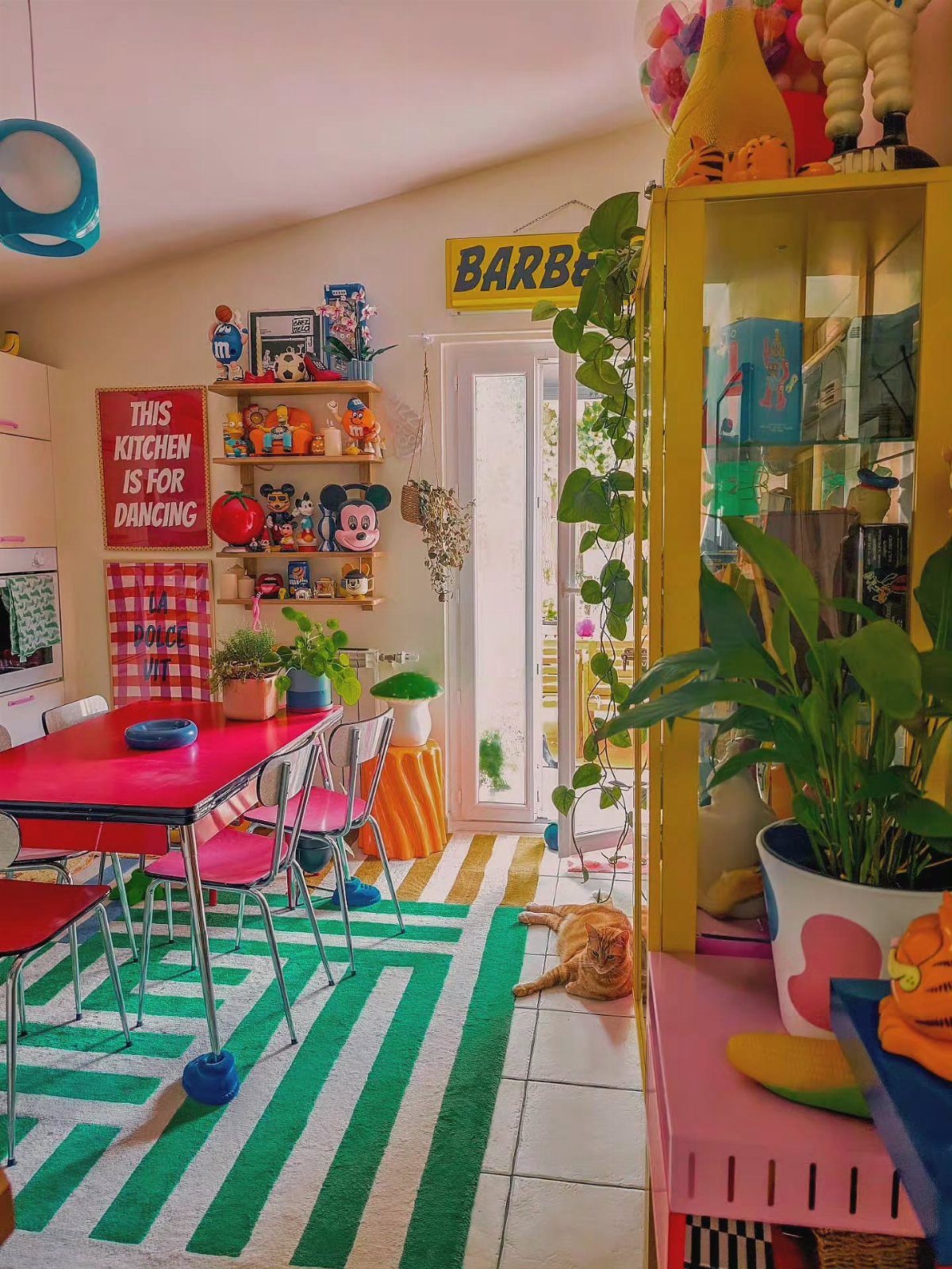 22 Apt Kitchen Ideas to Maximize Style and Function 15 Bright orange kitchen walls with a red table, pink chairs, and eclectic colorful decor.