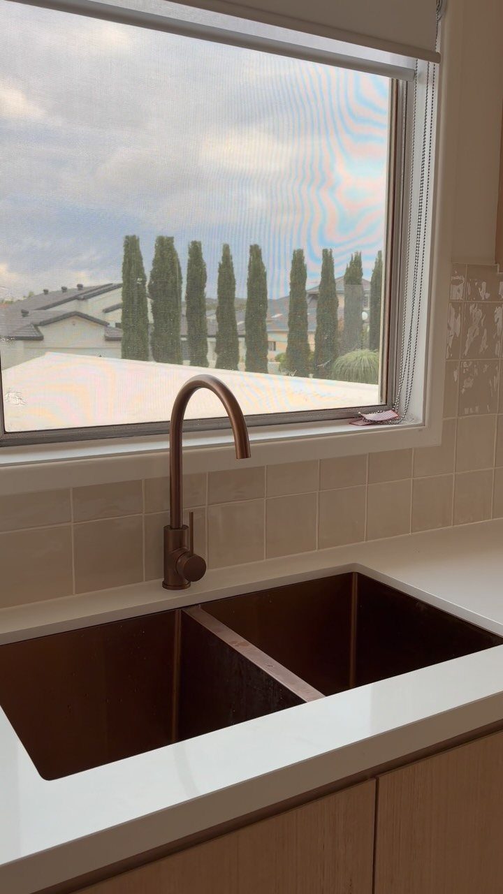 22 Apt Kitchen Ideas to Maximize Style and Function 10 White glossy tile backsplash and bronze faucet by a window overlooking cypress trees.