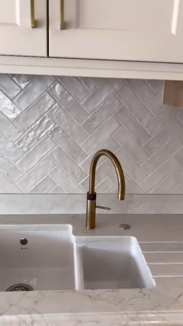 22 Apt Kitchen Ideas to Maximize Style and Function 11 White herringbone tile backsplash with a gold faucet and white kitchen cabinets.