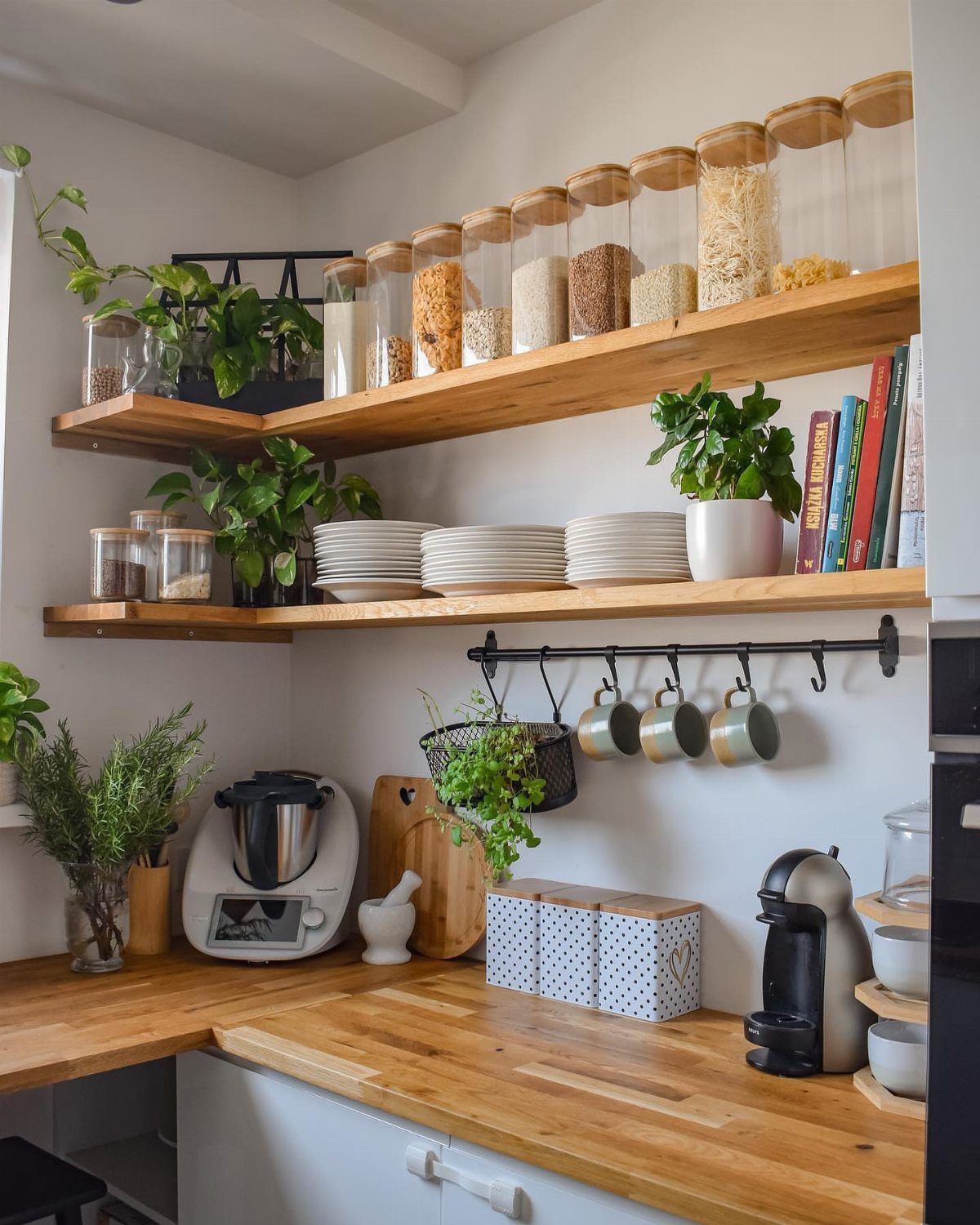 22 Apt Kitchen Ideas to Maximize Style and Function 2 Wooden wrap-around open shelves in a kitchen holding jars, plates, and plants.