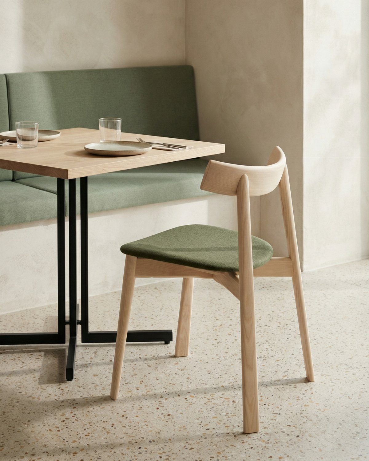 Ash wood dining chair with green seat next to a restaurant table and banquette.