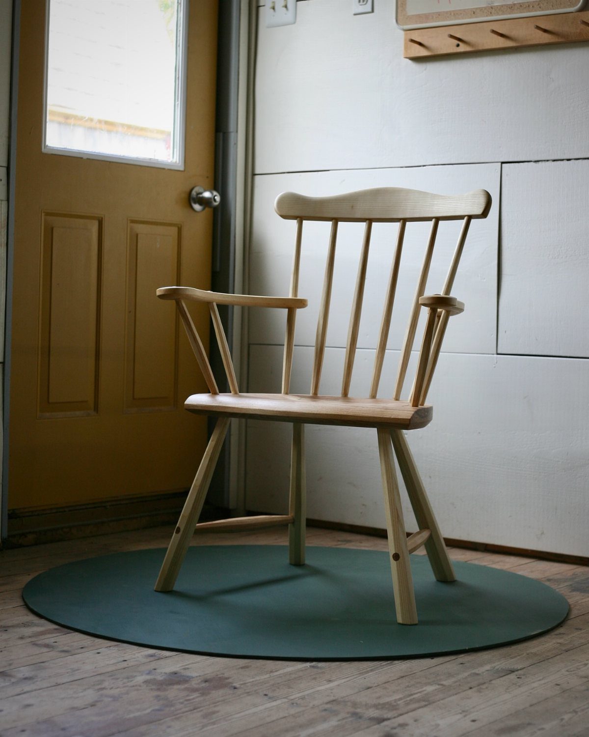 Ash wood dining chair with armrests and spindle back on a green mat.