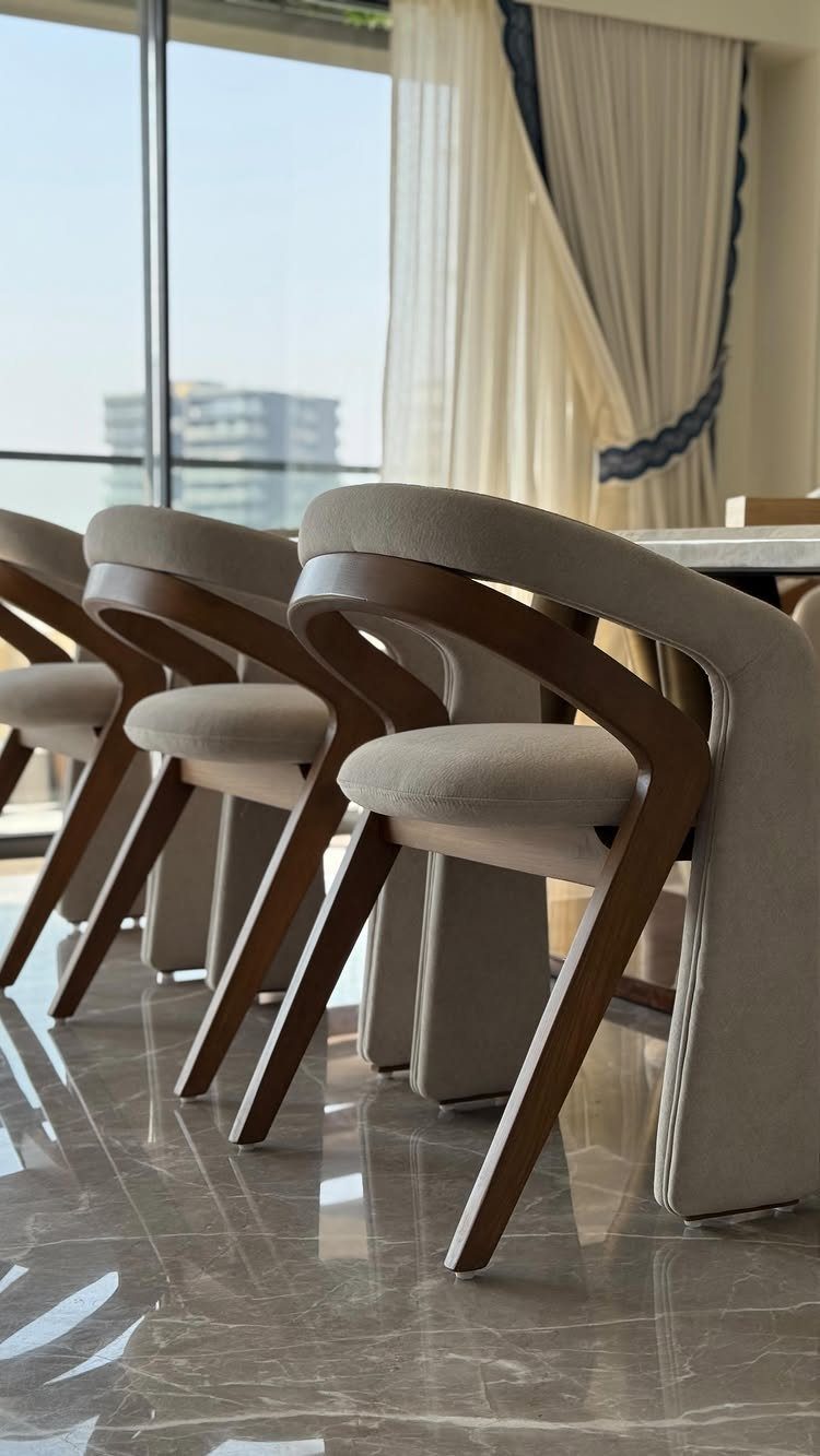 Modern dining chairs with curved wooden frames and beige upholstery in a bright room.