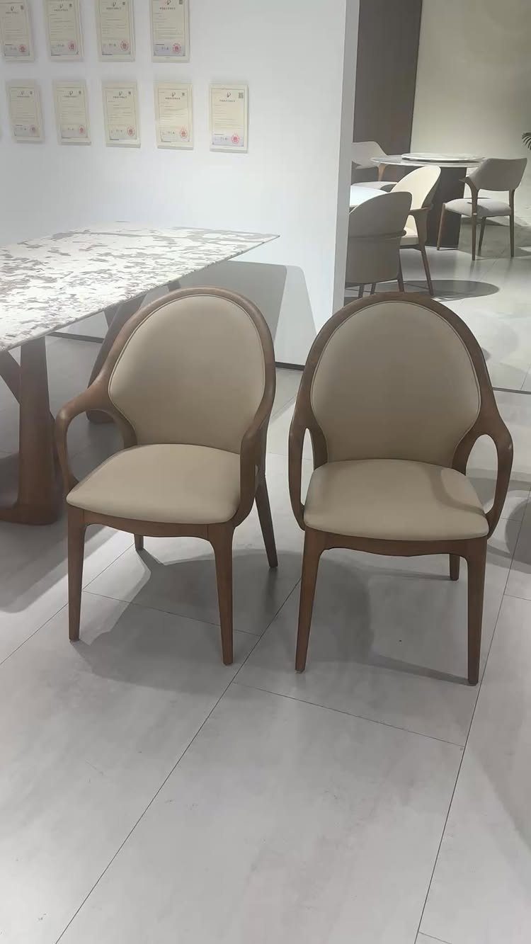 Two light-brown wooden dining chairs with beige upholstery and curved backs.