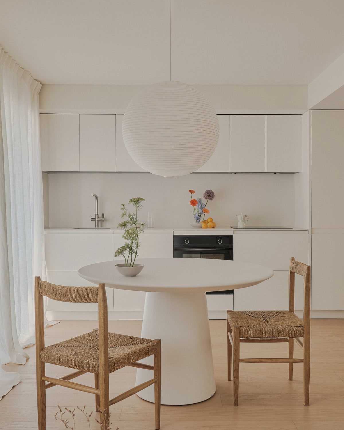 Wooden dining chairs with woven seats around a white pedestal table in a kitchen.