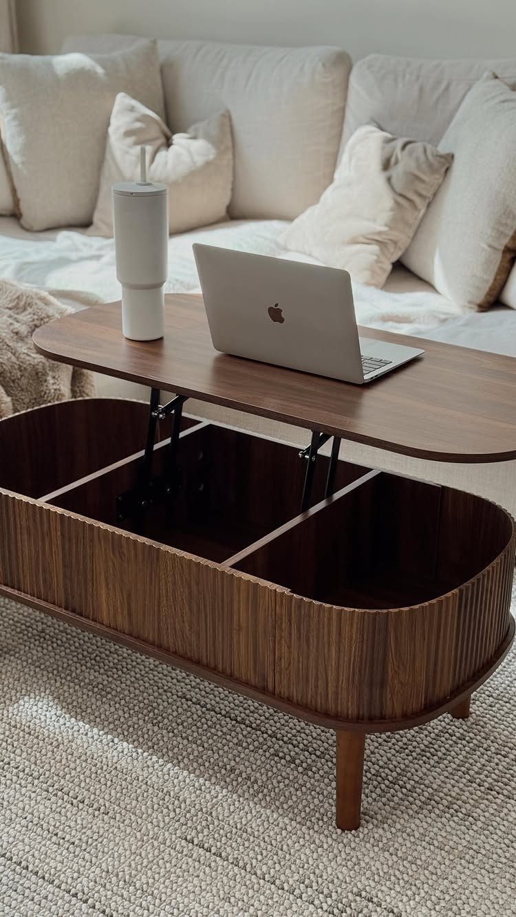 Wooden lift-top coffee table with open storage compartments, laptop, and white sofa background.