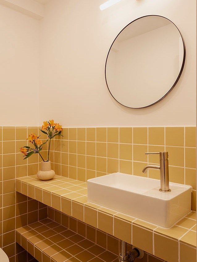 Yellow square tiles on a bathroom wall and vanity with a white sink.