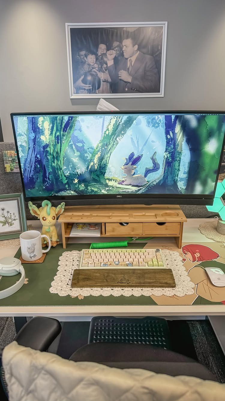 Computer monitor displaying blue and green forest art on a decorated desk setup.