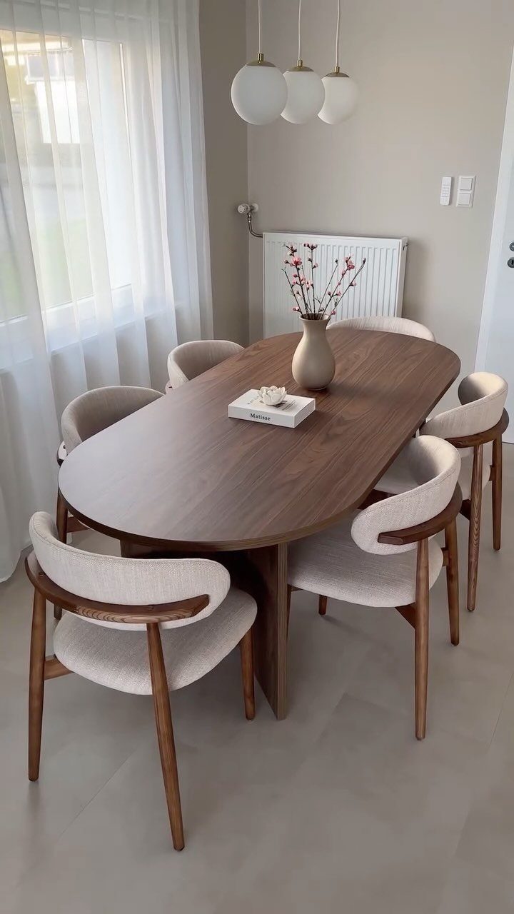 Oval dark wood dining table with cream upholstered chairs in a neutral room.