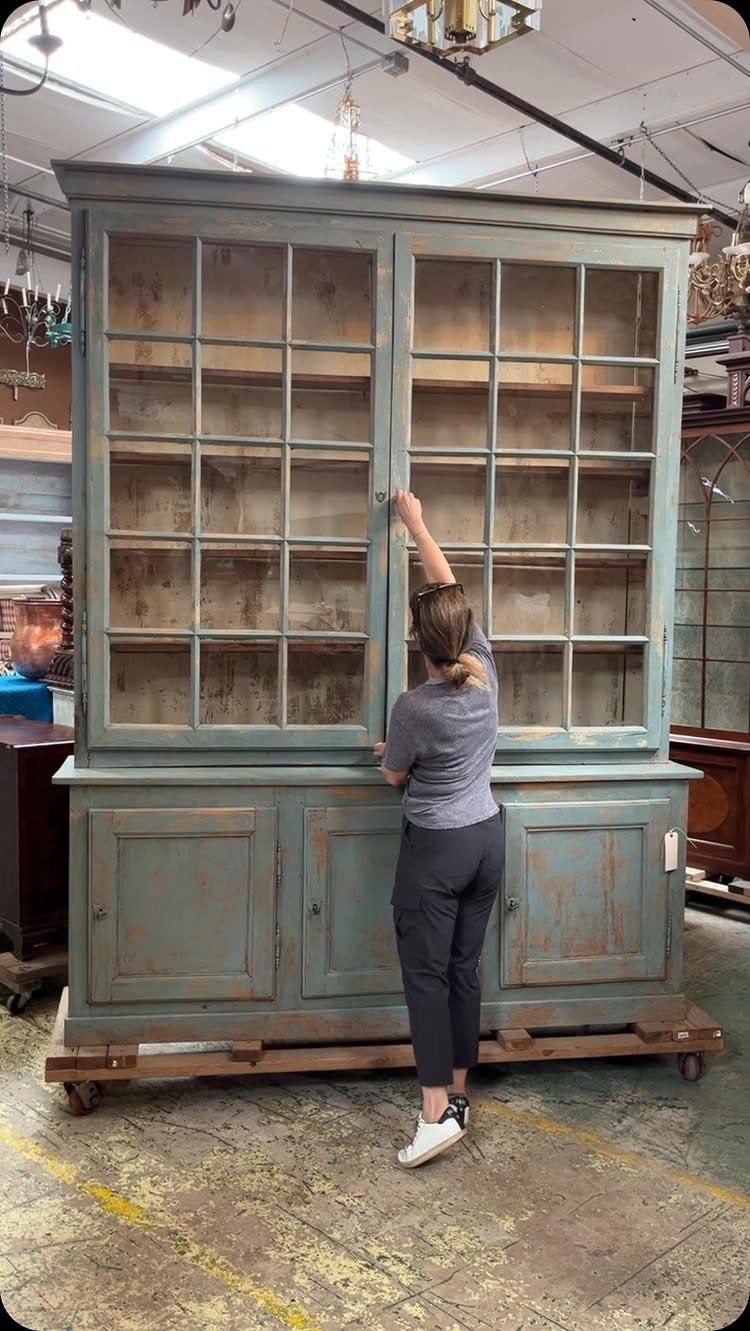 Light blue-grey distressed wooden hutch with glass doors in a furniture workshop.