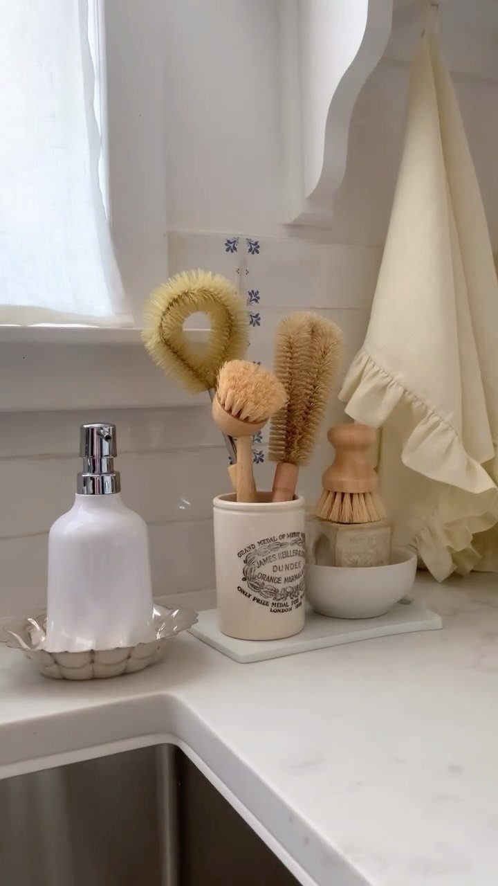 White kitchen counter with wooden dish brushes, soap dispenser, and ruffled white cloth.