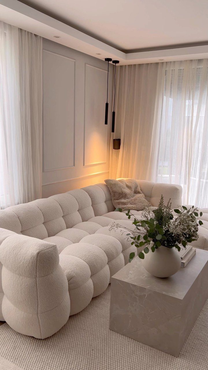 White modular tufted sofa in a neutral room with stone coffee table and greenery