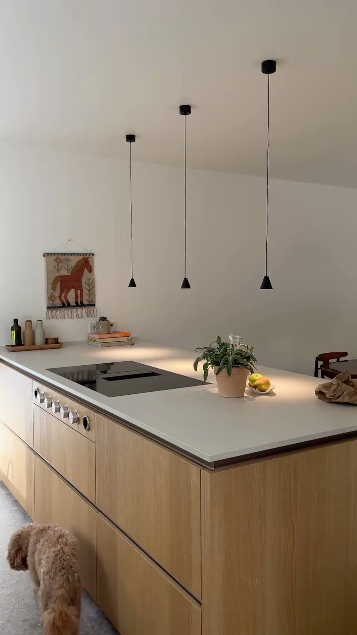 Modern kitchen island with white countertop, light wood cabinets, and black pendant lights.