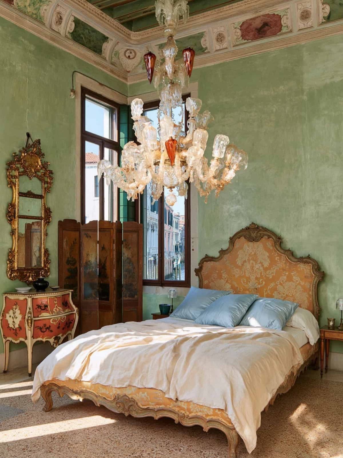 Ornate bedroom with a large glass chandelier, gold furniture, and light green walls.