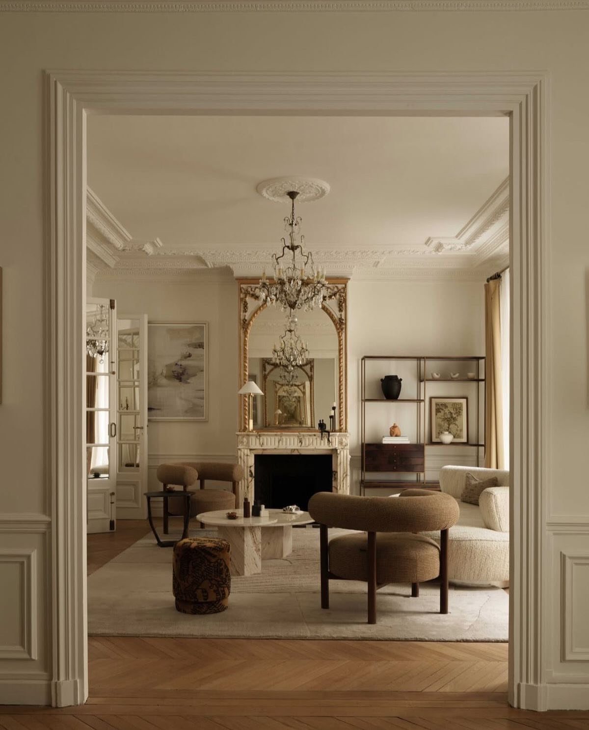 Luxurious neutral living room with crystal chandelier, ornate gold mirror, and herringbone floors.