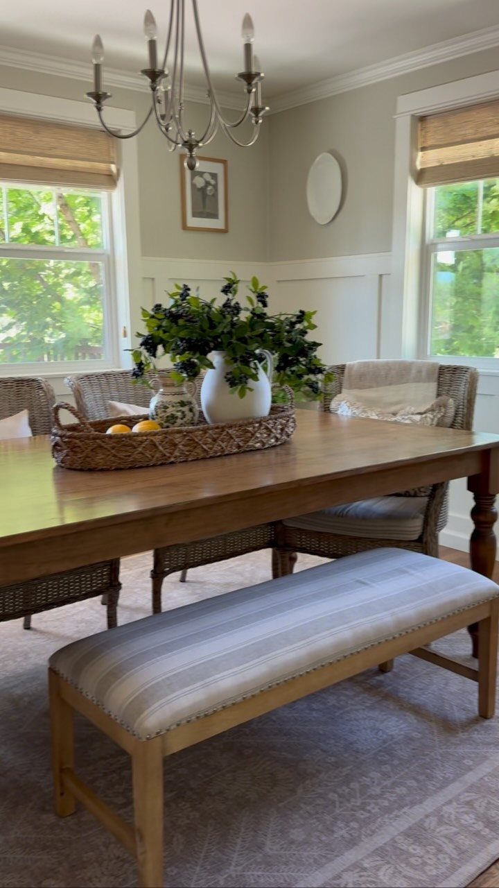 Wooden dining table with striped bench and wicker chairs in a bright room.