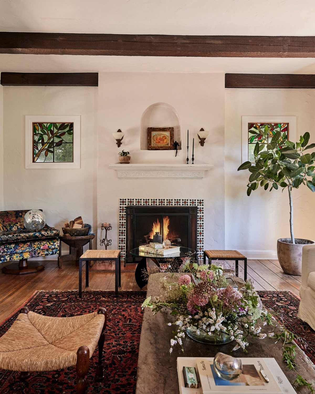 Living room with dark ceiling beams, tiled fireplace, and rustic woven furniture.