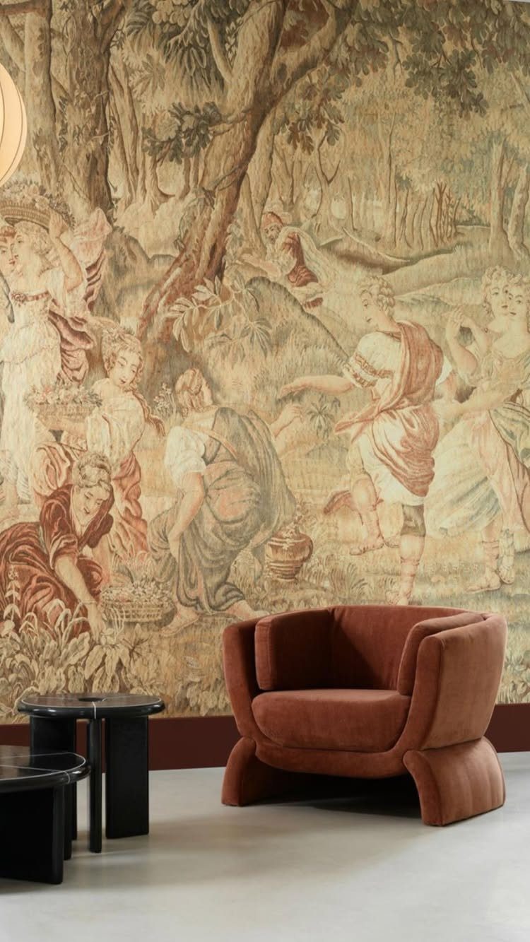 Large classical forest tapestry on a wall with a rust velvet armchair.