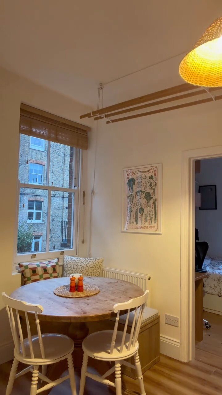Round wooden table with white chairs and a built-in bench breakfast nook by a window