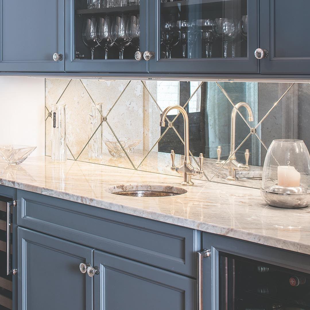 Mirrored backsplash with diamond grid reflecting a faucet and marble kitchen countertop.