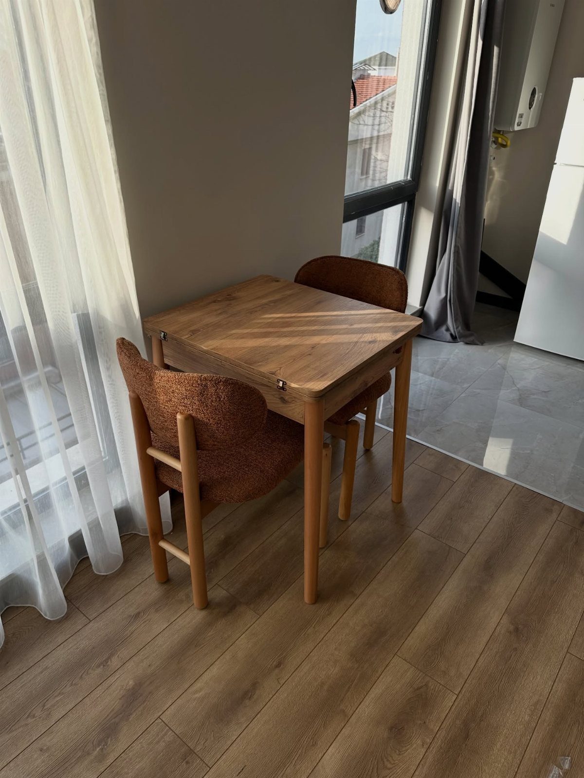 Small wooden square table with two brown chairs next to a window