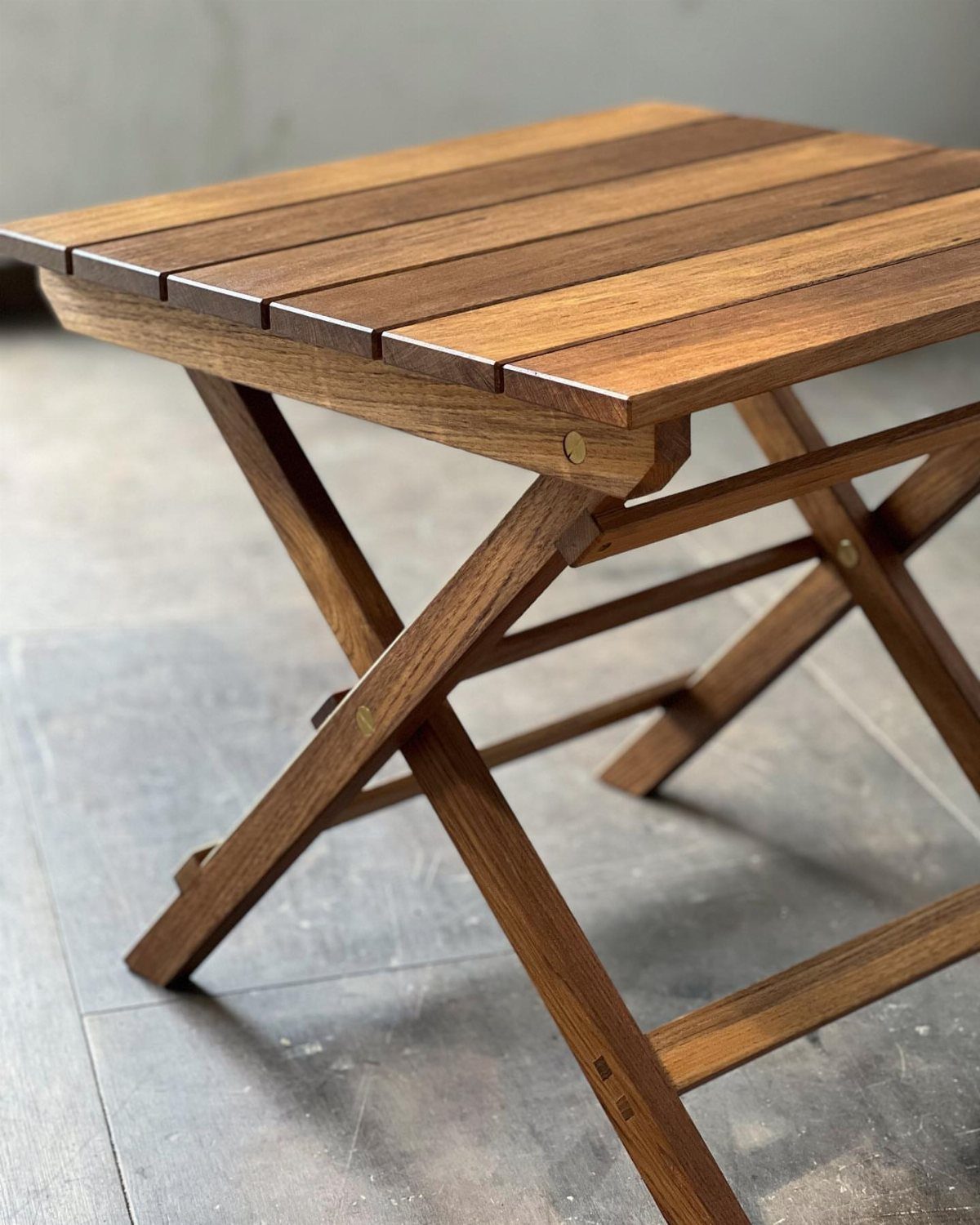 Small wooden folding table with slatted top and X-shaped legs on gray floor.