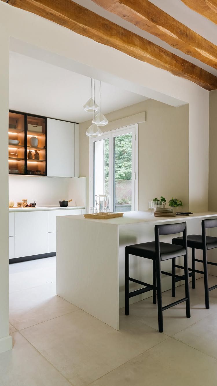 Modern white kitchen with glass-front upper cabinets and a white island with black stools.