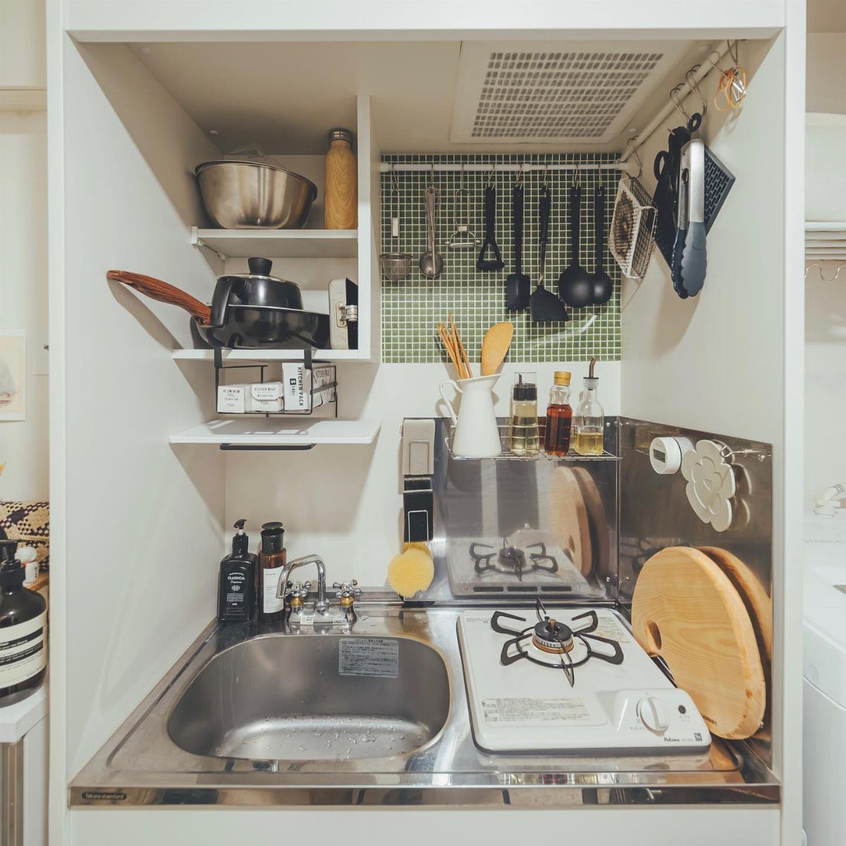 Small kitchen nook with white open shelves, stainless steel sink, and gas stove.
