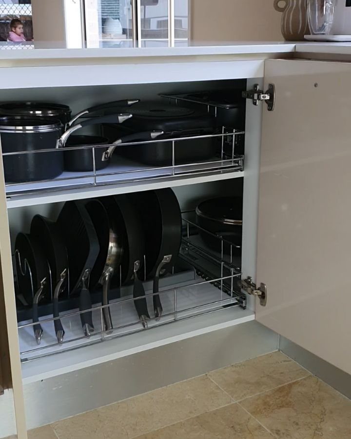 Open beige kitchen cabinet with two pull-out wire drawers holding black cookware.