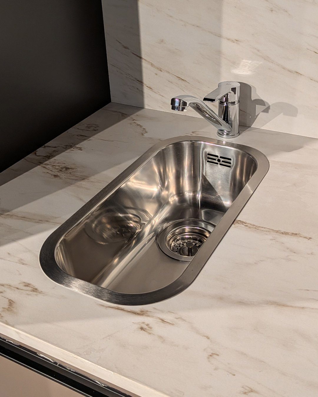Stainless steel single-bowl sink with chrome faucet on a white marble countertop.
