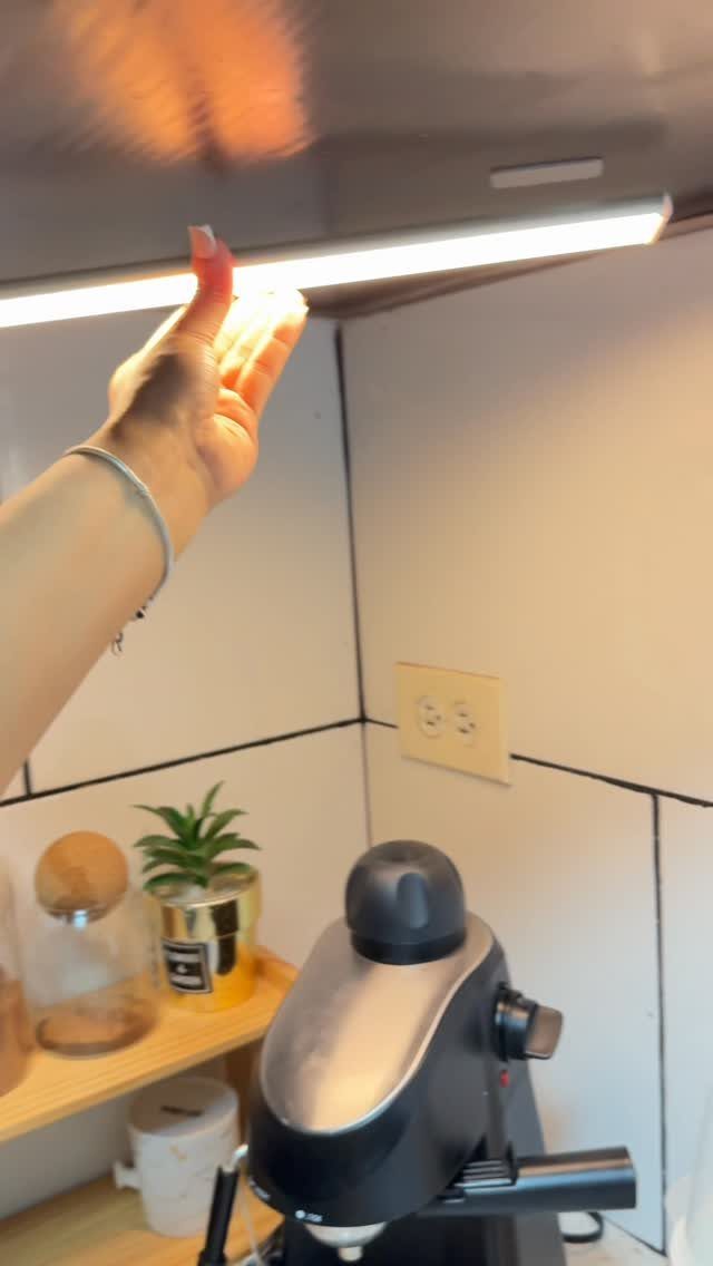 Hand touching a bright white LED light strip under a dark kitchen cabinet