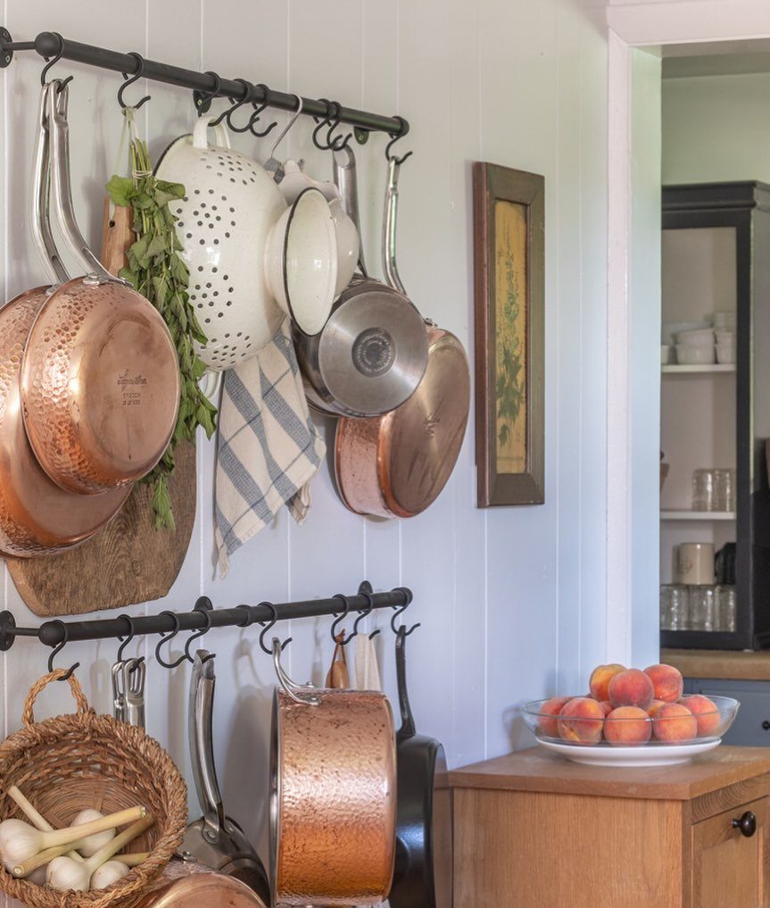 Wall-mounted pot racks holding copper cookware and a colander on a white wall.