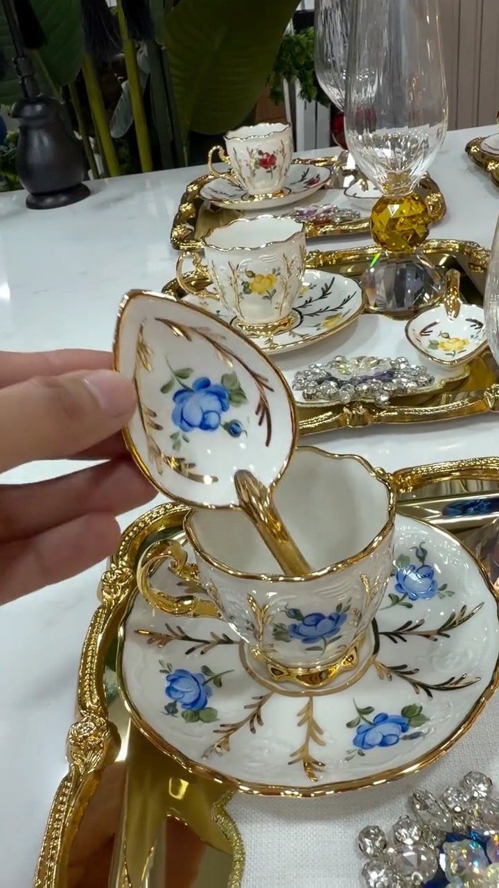 Fancy Dinnerware Set Ideas for 2026 Tables (28 Styles) 26 Ornate white porcelain teacup and saucer with blue roses and gold trim on gold trays.