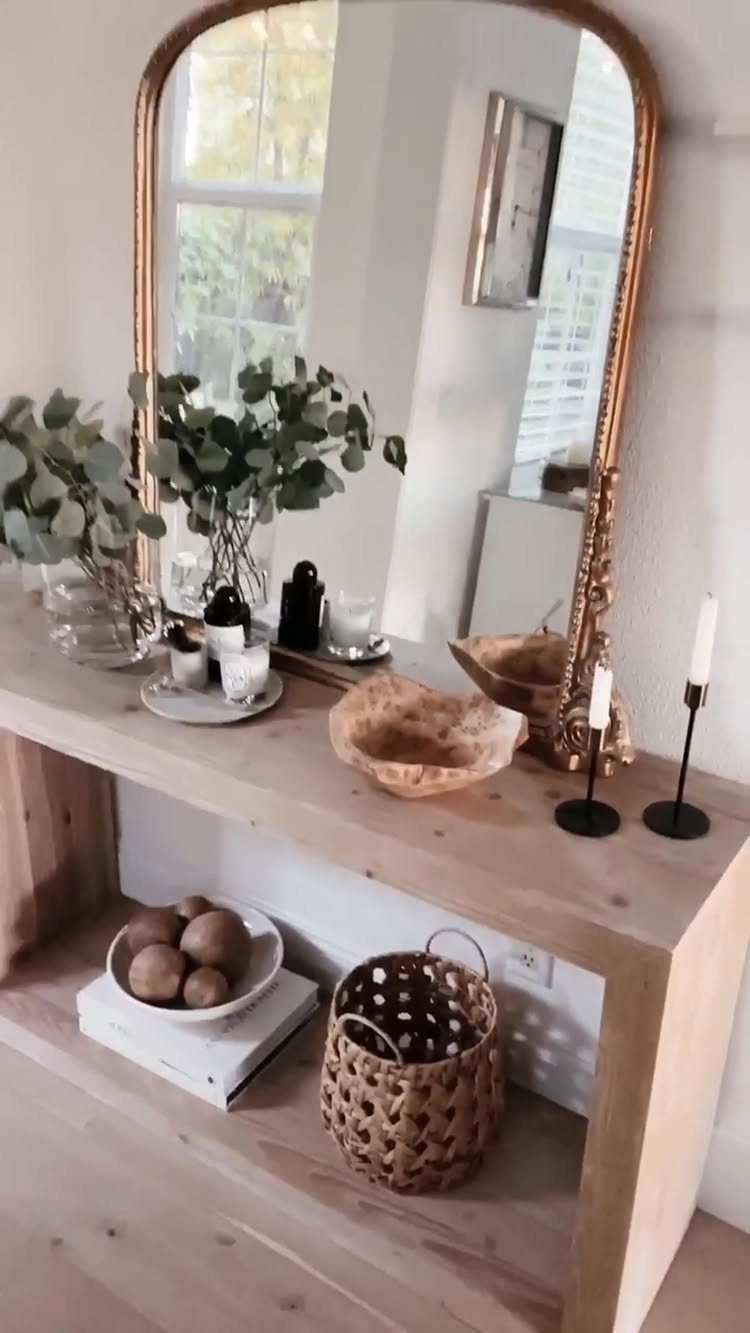 9 Gold Accent Living Room Ideas for Every Style 3 Arched gold-framed mirror leaning on a light wood console table with greenery.