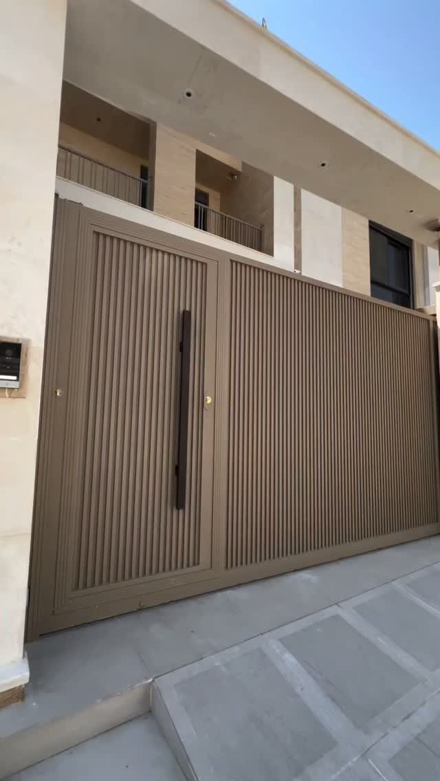 Beige modern home exterior with a large ribbed metal gate and minimalist walls.