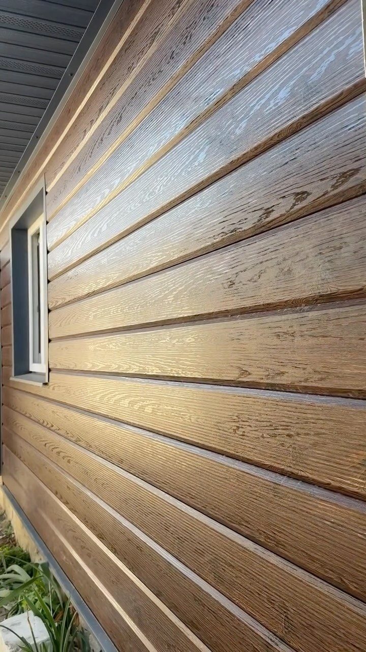 Brown horizontal wood-grain siding on the exterior wall of a house with a window.