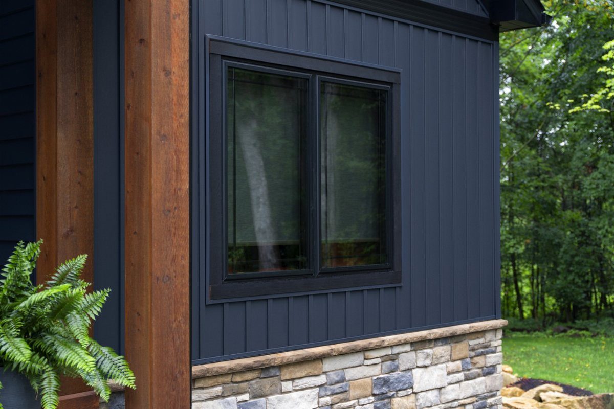 Modern house exterior with dark blue siding, stone veneer, and a wooden pillar.