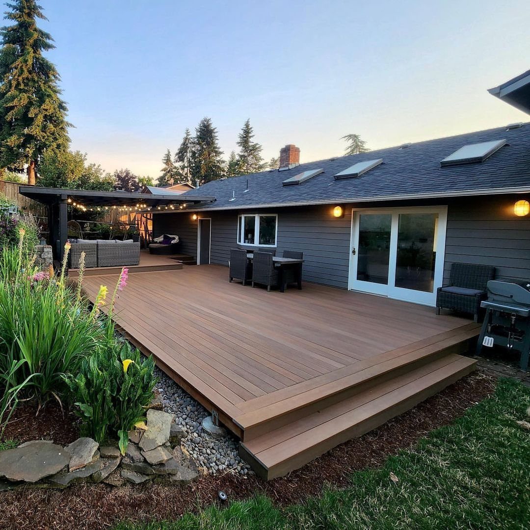 Large brown composite wood deck with outdoor furniture and pergola attached to gray house.