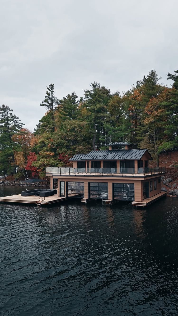 Two-story boathouse with tan walls and dark roof on a lake during autumn.