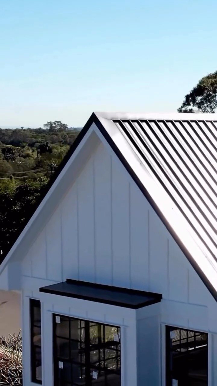 Dark grey standing seam metal roof on a white house with vertical siding.