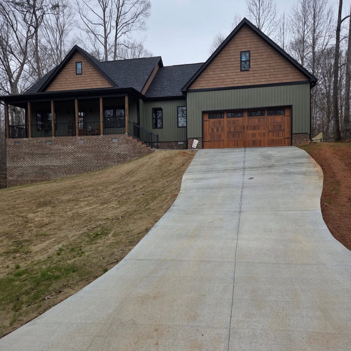 Modern house with olive green siding, brown gables, and a concrete driveway.