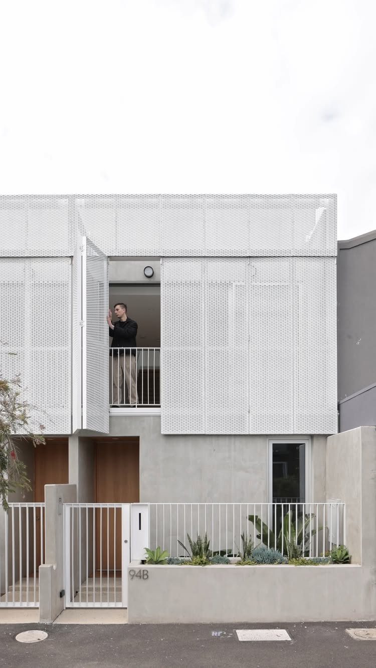 Modern two-story house with white perforated metal screens and grey concrete exterior walls.