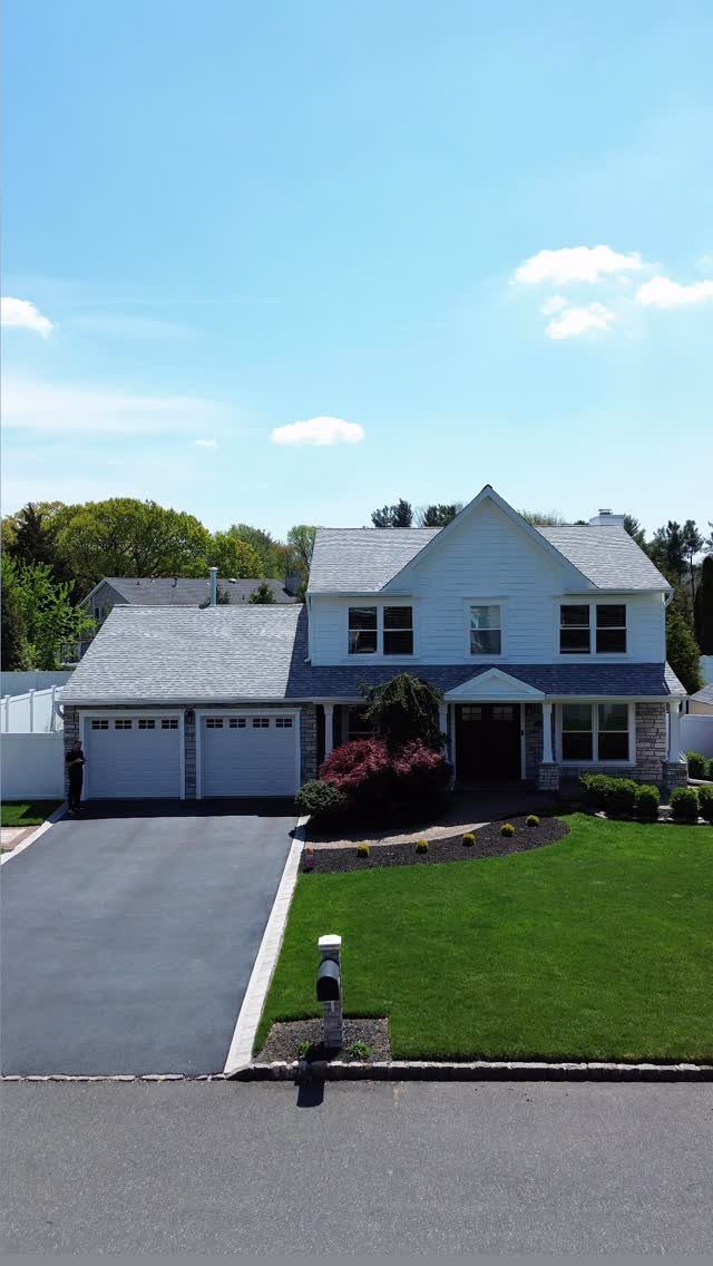 White two-story house with vinyl siding, gray roof, and a manicured green lawn.