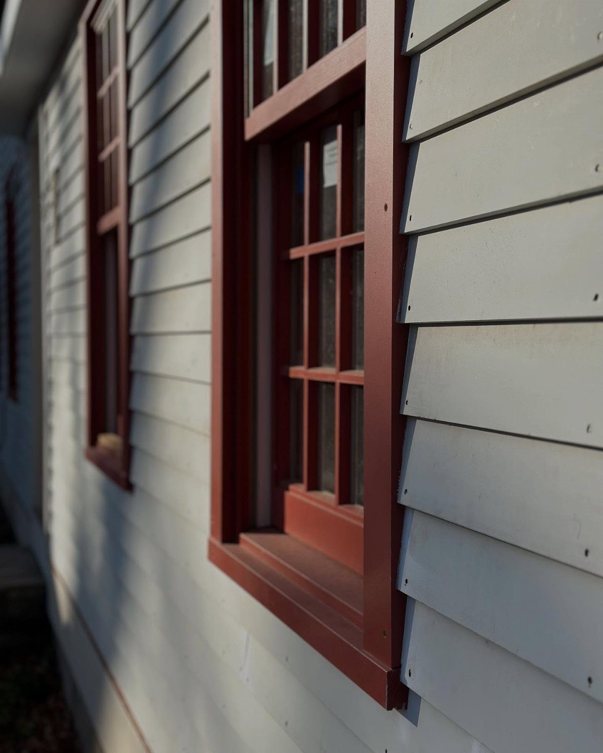 Light gray wood clapboard siding with a reddish-brown window frame on a house.