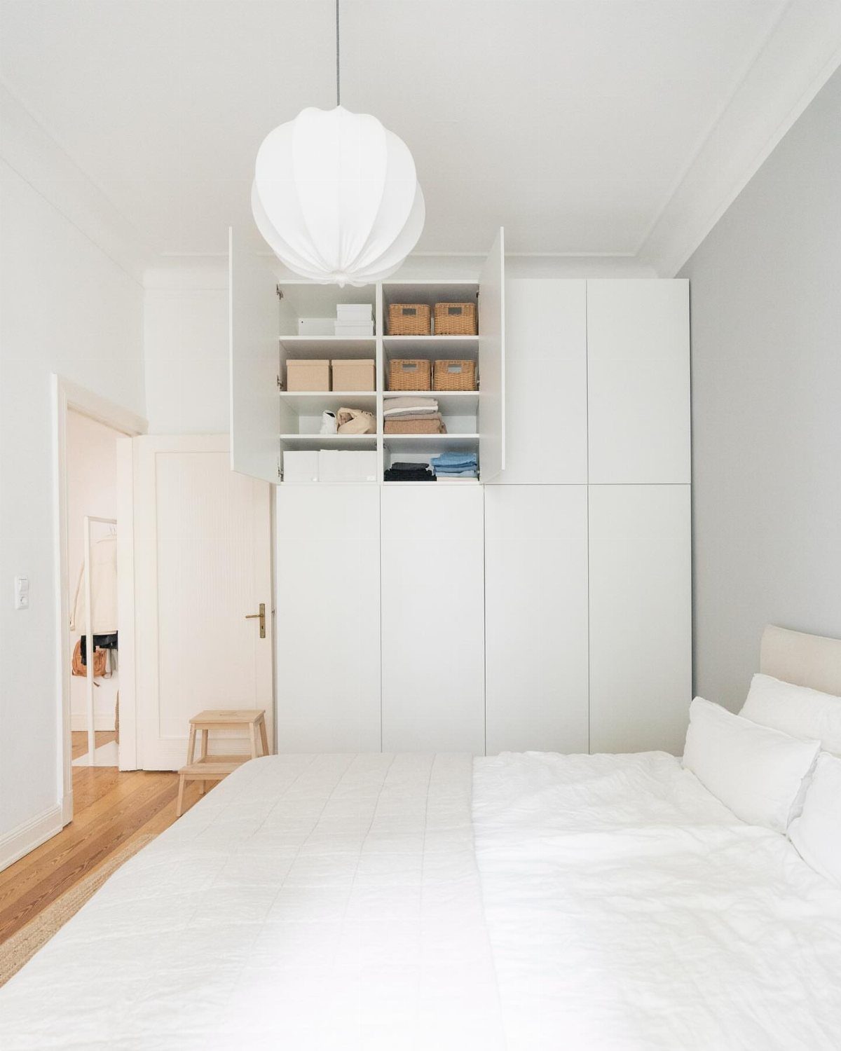 White modular wardrobes with overhead bridging cabinets in a bright, modern bedroom