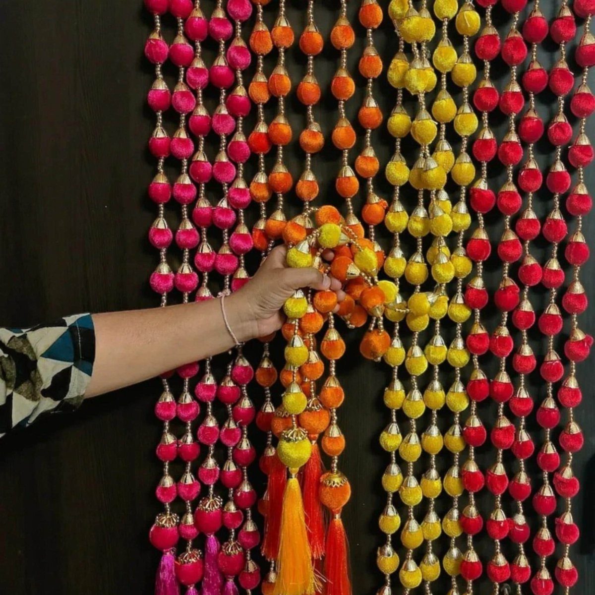 Indian Room Decor: 37 Ideas From Textiles to Wall Hangings 18 Colorful pink, orange, and yellow tassel garlands hanging against a dark brown wall.
