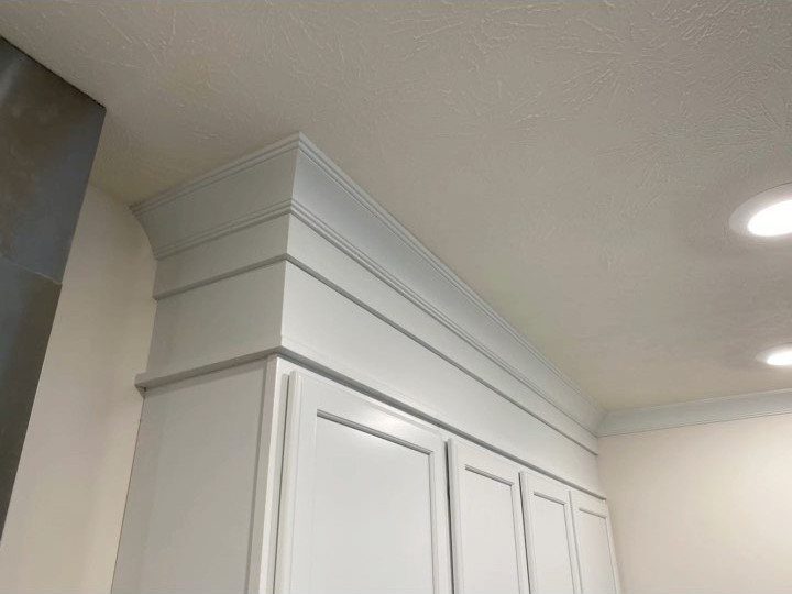 White kitchen cabinets featuring tiered crown molding extending up to the ceiling.