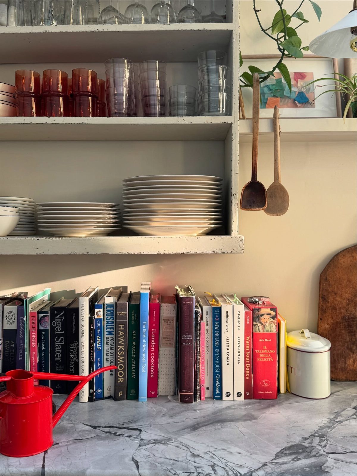 Cookbooks lined up on a marble countertop below white open kitchen shelves.