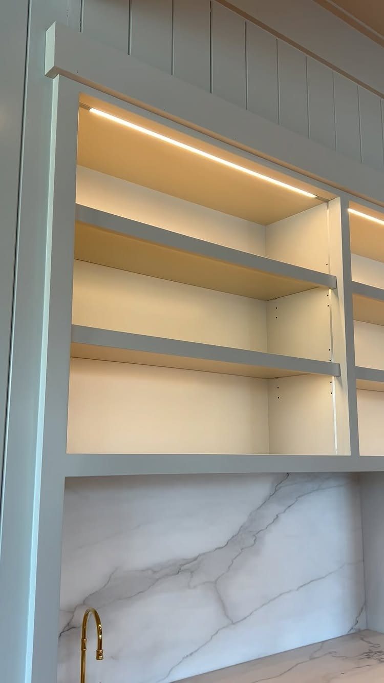 White built-in kitchen shelving with integrated LED lighting above a marble countertop