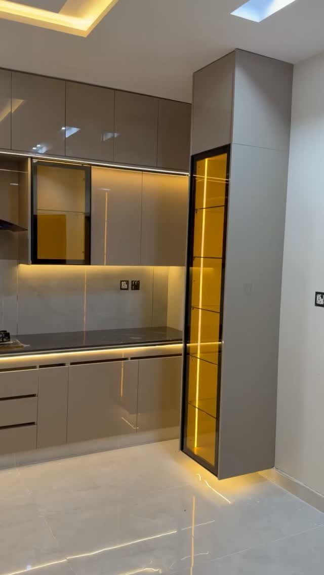Taupe kitchen cabinets extending to the ceiling with a backlit yellow glass display cabinet.